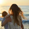 Mère portant son enfant face à la mer au coucher du soleil