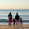 Famille de quatre personnes face à la mer sur une plage au coucher du soleil
