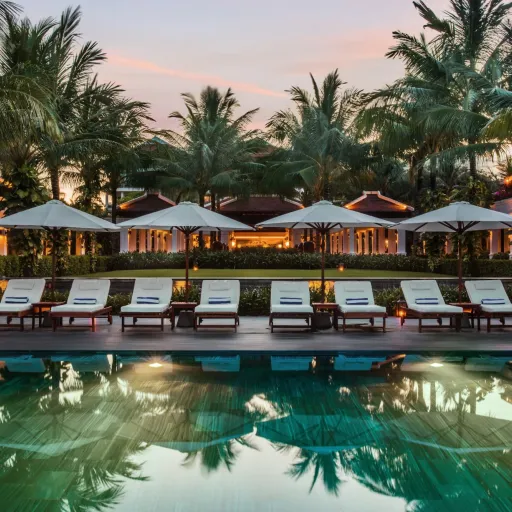 Piscine et transats d'un hôtel resort entre les palmiers au crépuscule
